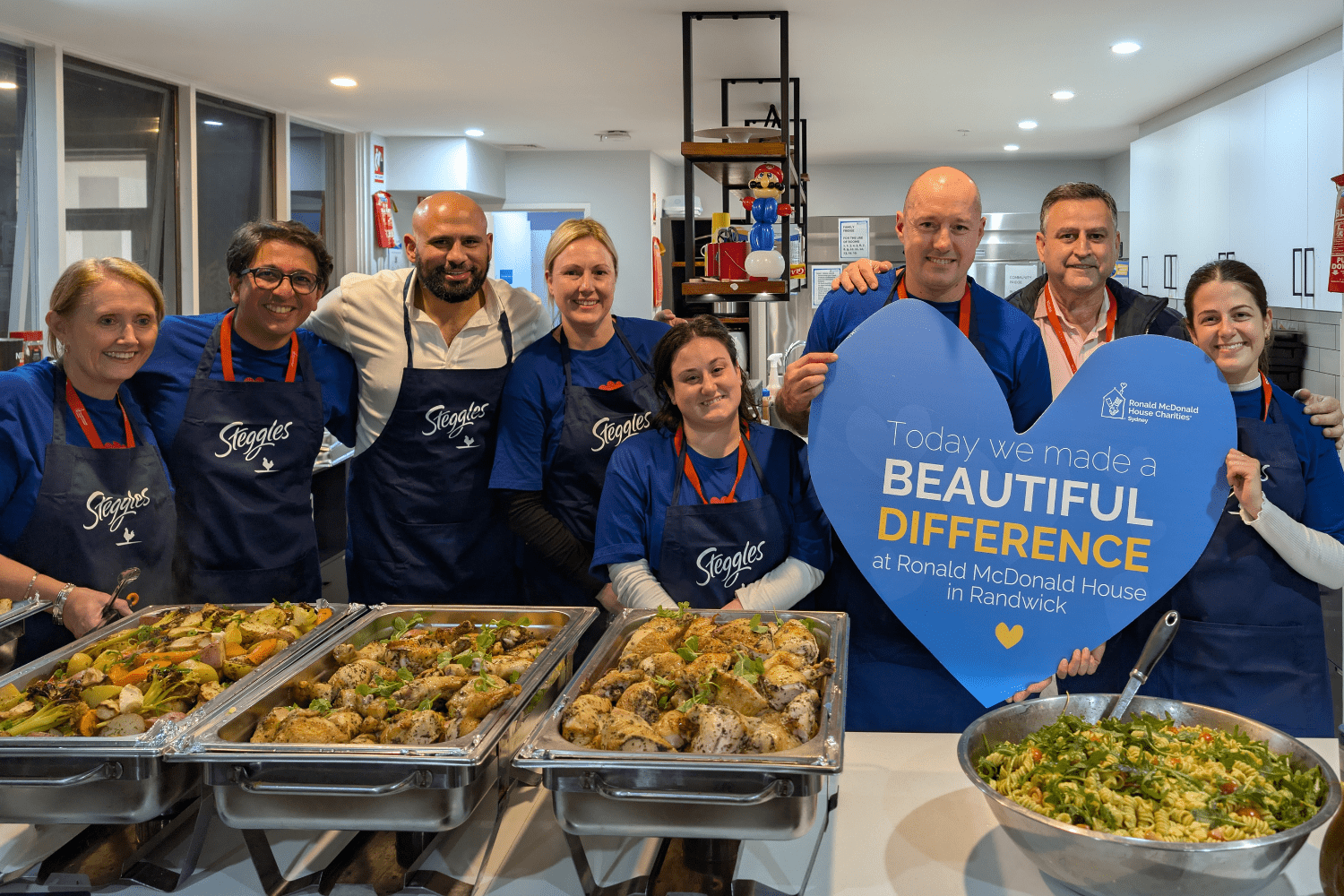A group of Steggles staff standing behind a large cook up of meals for families